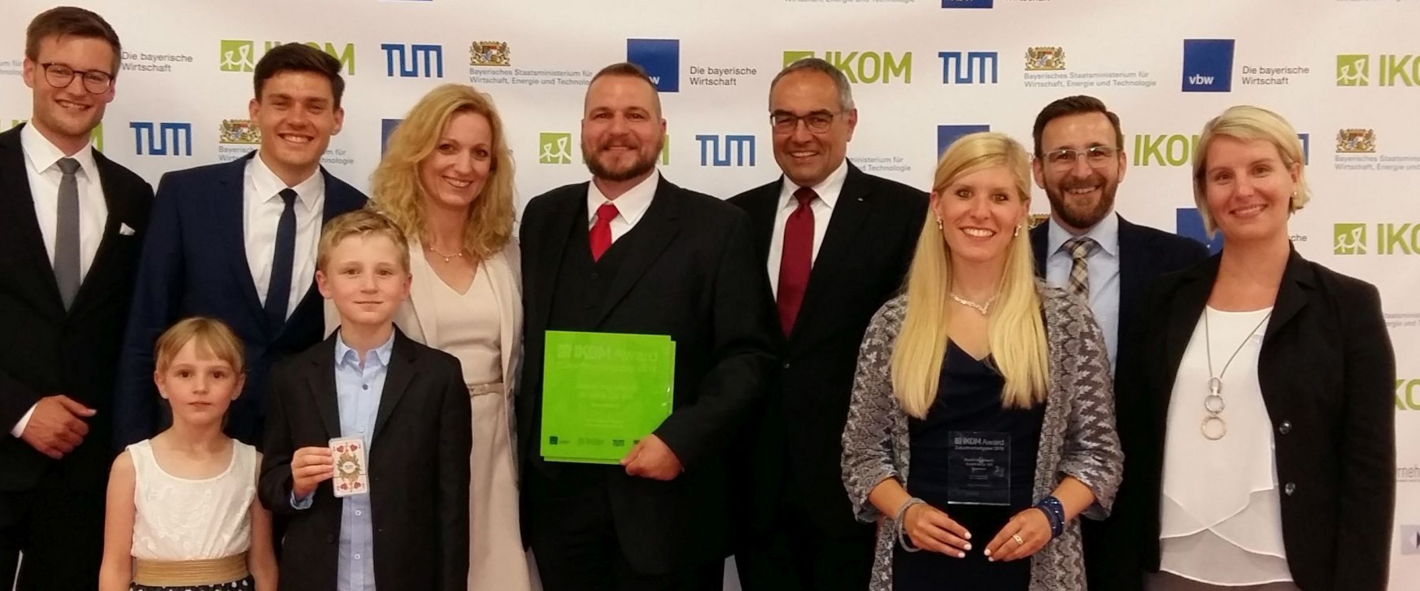 Gruppenbild vor IKOM-Fotowand:  v.l.n.r.: Marius Beller und Niclas-Alexander Mauss (IKOM/TUM), Susanne Duschl, Andreas Duschl, TUM-Kanzler Albert Berger, Mitarbeiter Stefanie Gschwendtner, Alexander von Schneyder und Michaela Erben, vorne Leni und Anian Duschl.