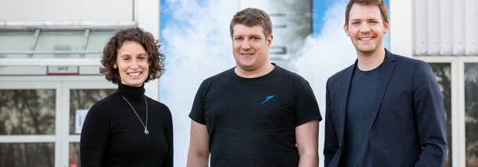 Portrait picture of Lucrezia Veggi, Josef Fleischmann and Daniel Metzler in front of the production halls of Isar Aerospace.