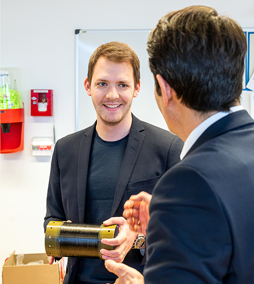 Daniel Metzler holding a rocket component talks to President Thomas F. Hofmann.