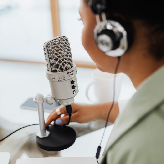 A woman wearing headphones speaks into a podcast microphone.