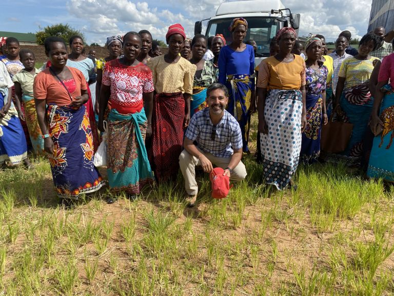 Eine Gruppe von bunt gekleideten Frauen steht auf einem Feld. In der ersten Reihe kniet Francisco Obreque. Alle lächeln.